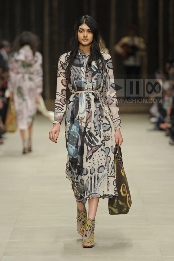 A model walks the runway in a long-sleeved, midi-length dress with an abstract print, cinched at the waist with a thin belt.