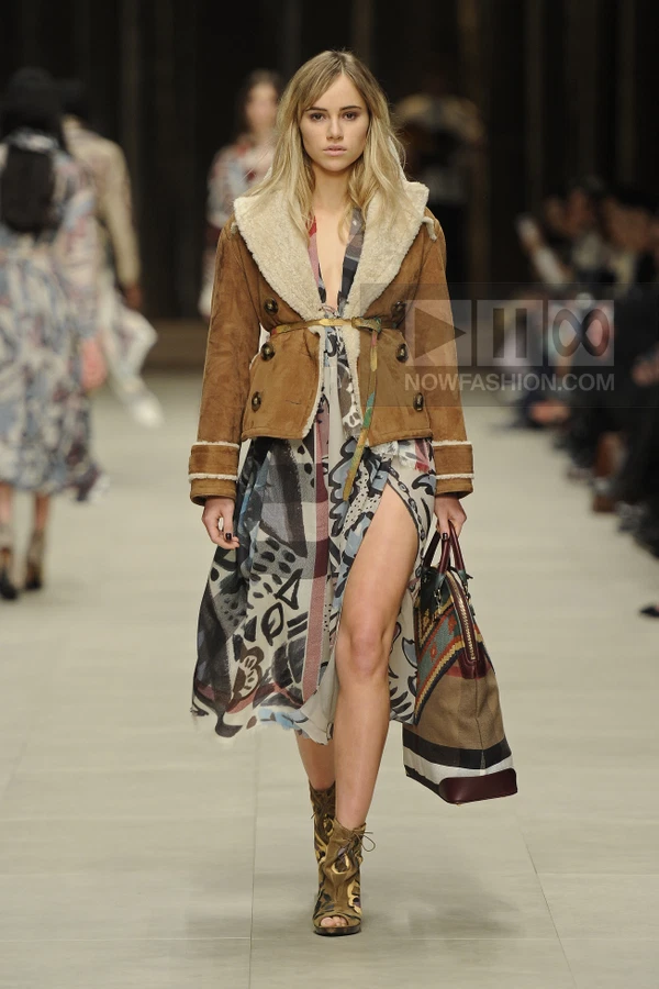 Model walking on runway wearing a brown shearling-lined jacket over a printed midi dress with a high side slit.