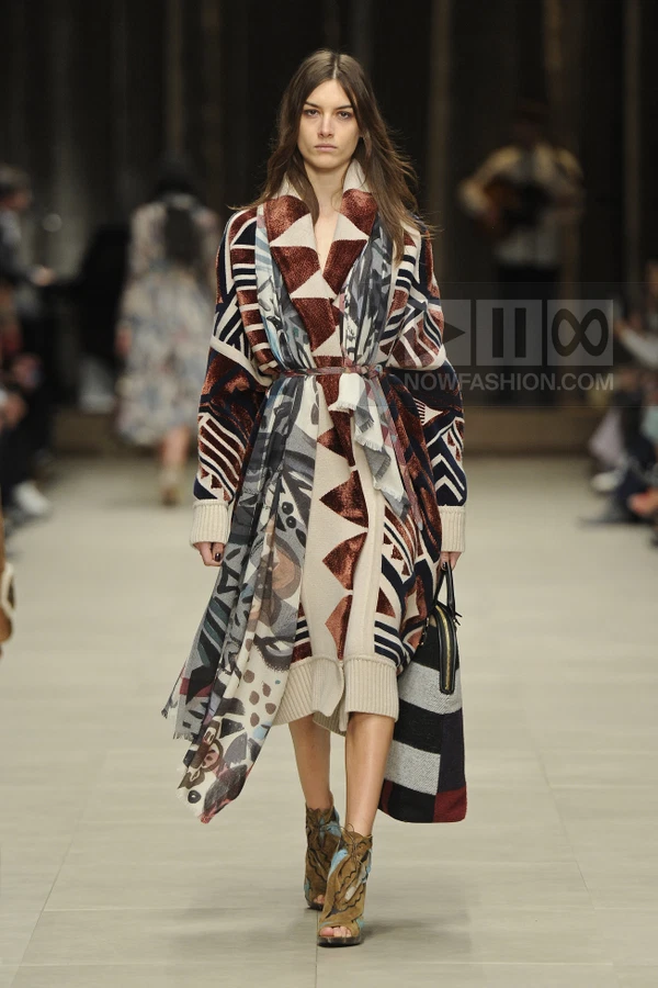 Model walking in a patterned knit coat, matching dress, and open-toe lace-up boots on a runway.