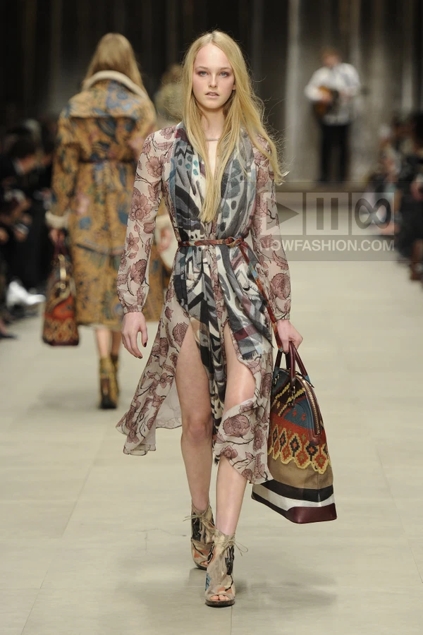Model walking in a floral chiffon dress with a patterned scarf, leather belt, and a large multi-colored tote bag.
