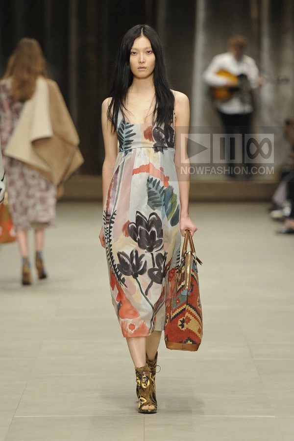 Model walking in a midi-length dress with a hand-painted floral print, carrying a patterned tote bag and ankle boots.