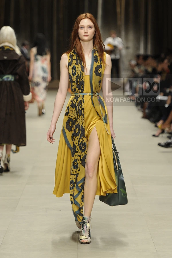 Model walking in a yellow midi dress with a floral scarf draped over the shoulder and belted at the waist.