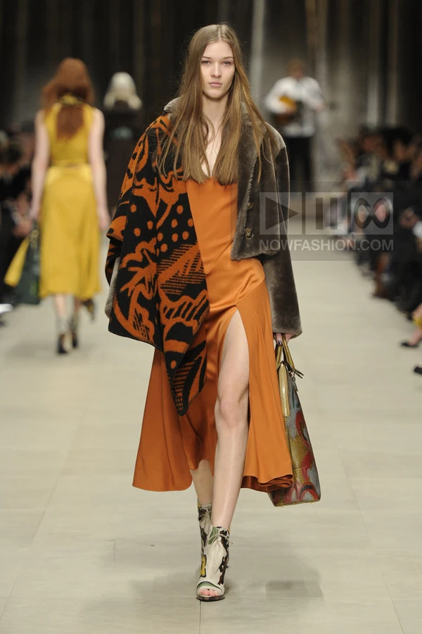 Model walking in a burnt orange slip dress with a high slit, layered under a brown shearling jacket and patterned shawl.