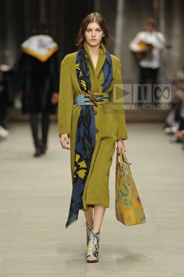 Model wearing a long olive mohair coat, a blue floral scarf, a wide buckled belt, and patterned peep-toe ankle boots.