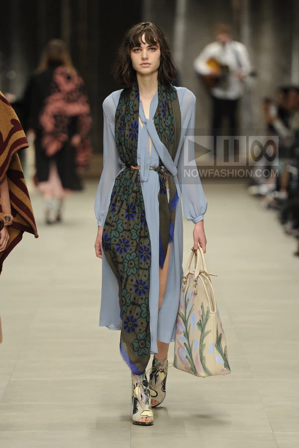 Model walking in a light blue midi dress with a floral scarf, holding a painted tote bag, wearing open-toe ankle boots.