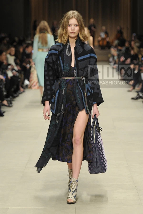 Model walking in a dark patterned coat over a floral midi dress, carrying a large tote bag and wearing peep-toe boots.