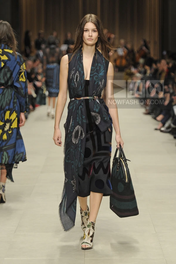 Model walking in a dark floral print midi dress with a matching scarf, belted waist, and patterned ankle boots.