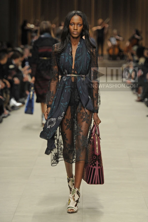 Model walking in a sheer black lace midi dress with a dark floral scarf, leather belt, and patterned ankle boots.