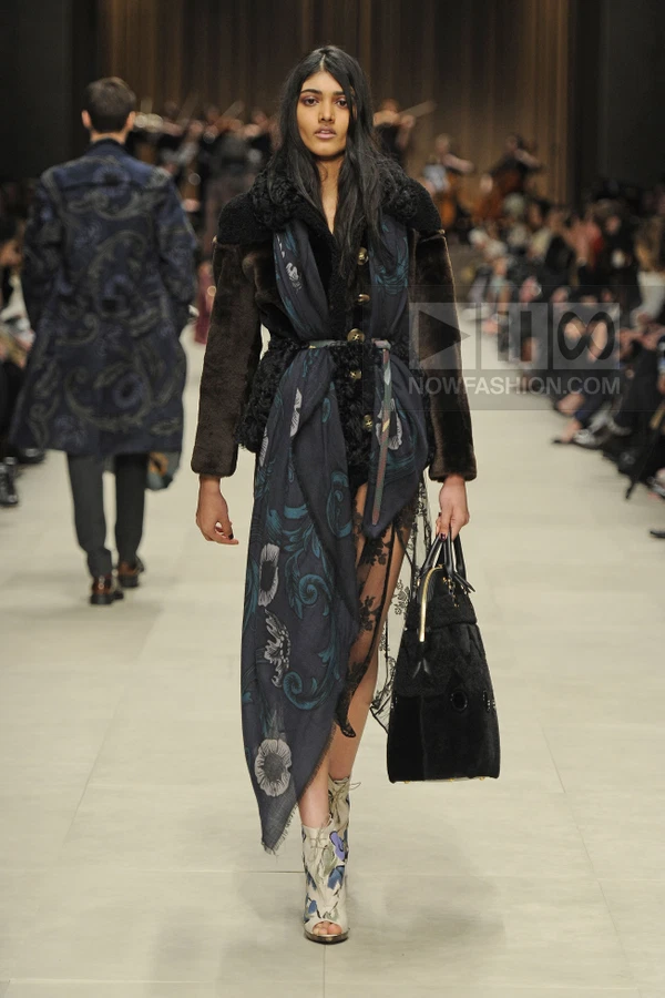 Model walking the runway wearing a dark fur-trimmed coat, a floral print scarf, lace tights, and peep-toe ankle boots.