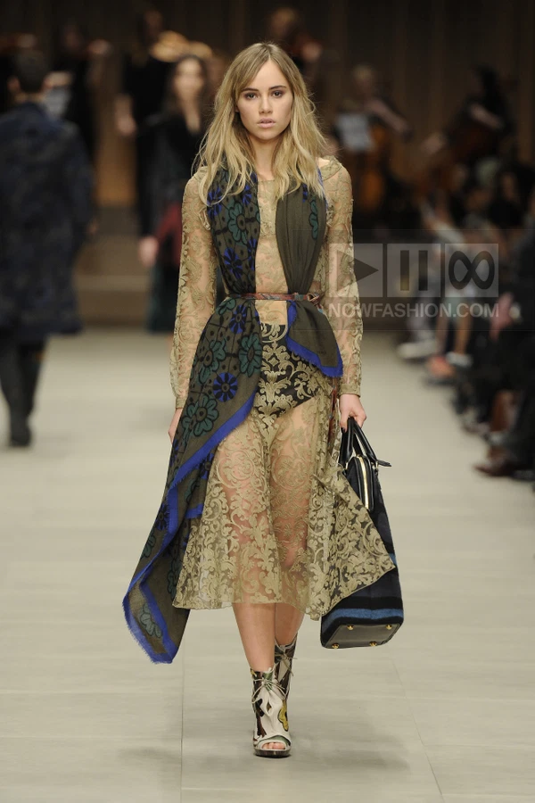 Model walking in a sheer olive lace midi dress with a floral printed scarf draped over the shoulders and a leather bag.