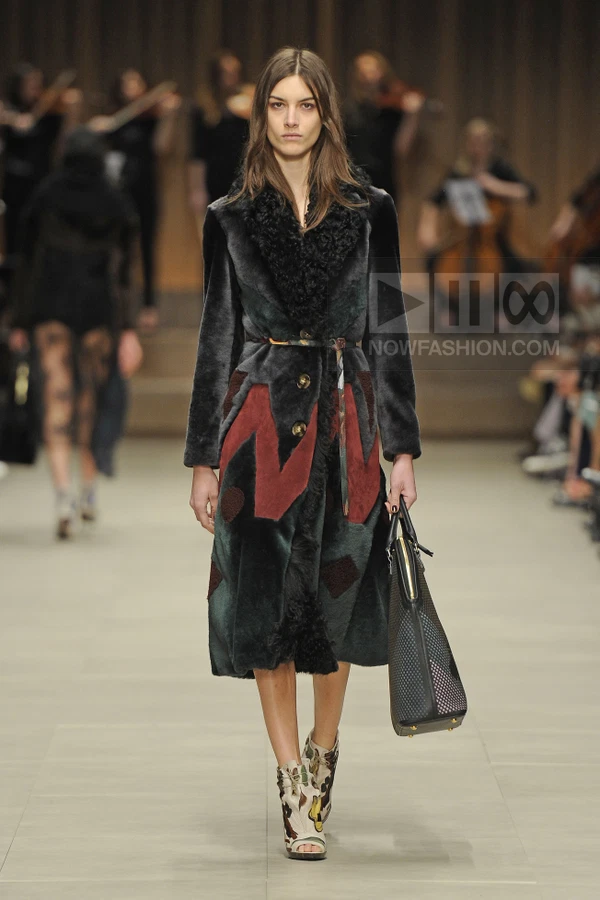 Model wearing a dark green and burgundy patterned shearling coat with a leather handbag and printed open-toe booties.