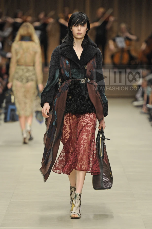 Model walking in a textured black coat, burgundy lace midi skirt, and patterned ankle boots on a runway.