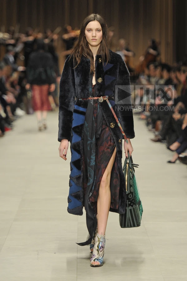 Model walking in a dark blue fur coat with blue geometric panels, worn over a floral print dress with a high side slit.