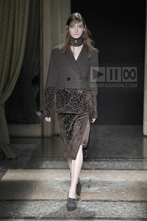 Model walking in a brown plaid and floral velvet jacket and skirt set with a high neck collar and dark suede pumps.