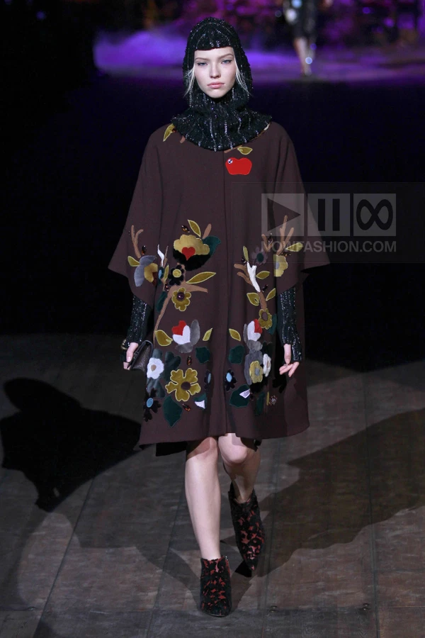 Model wearing a brown wool cape with floral appliques and a sequined black hood, paired with patterned ankle boots.