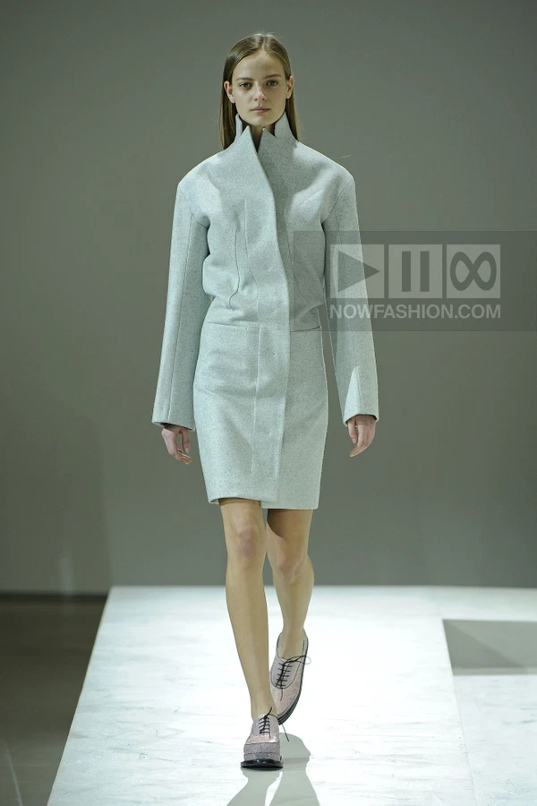 Model walking in a light blue wool coat dress with a high collar and lace-up shoes on a runway.