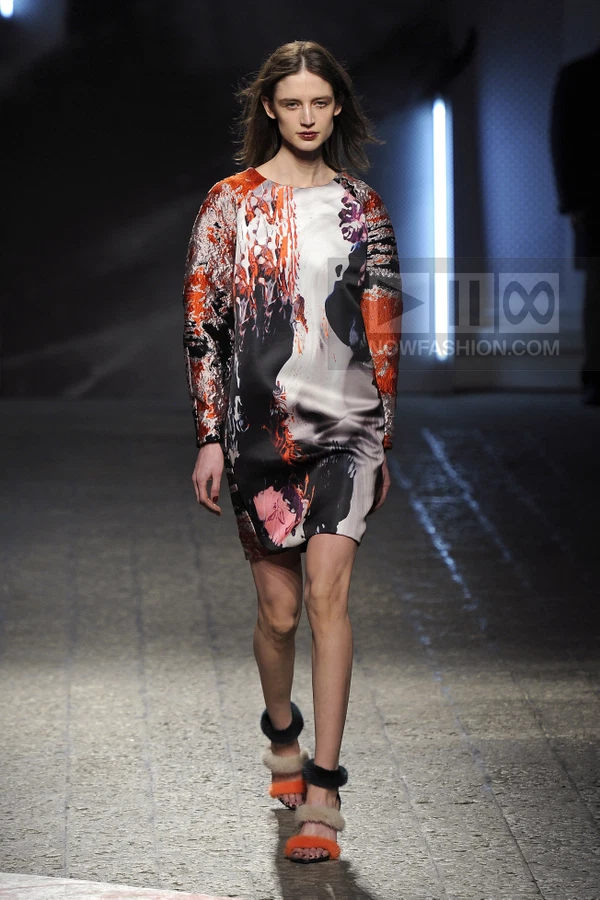 Model walking in a shift dress with abstract orange and black print, paired with fur-trimmed sandals on a runway.