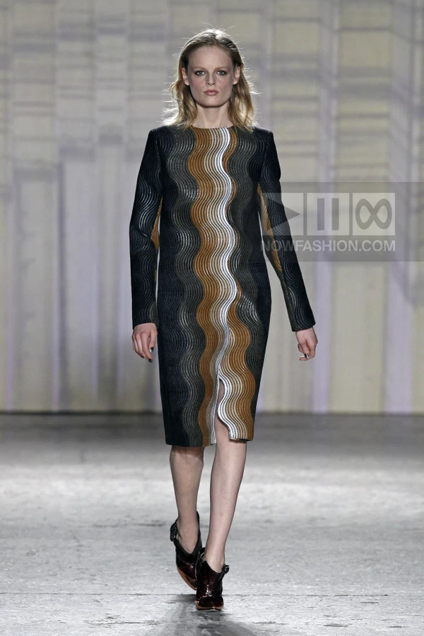 Model walking in a midi-length shift dress with a wavy, multi-colored vertical pattern and dark heeled shoes.