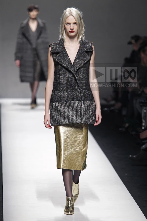 Model walking in a sleeveless charcoal tweed vest over a gold metallic midi skirt with matching gold ankle boots.