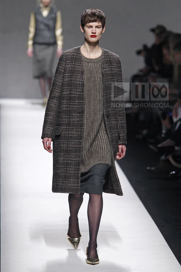 Model walking in a brown tweed coat over a ribbed knit sweater dress and dark gray skirt on a white runway.