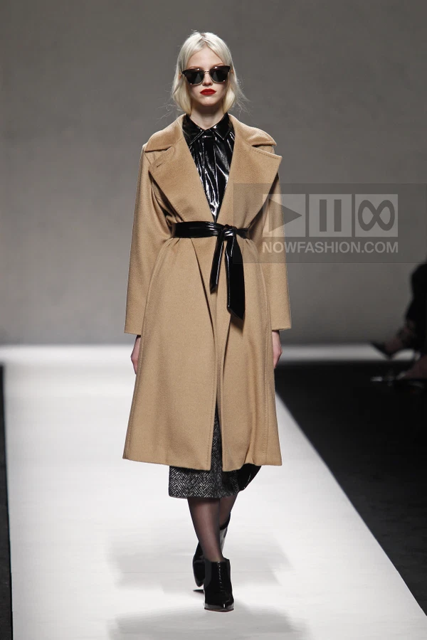 Model wearing a camel wool coat, black patent leather shirt and belt, herringbone skirt, and black ankle boots.