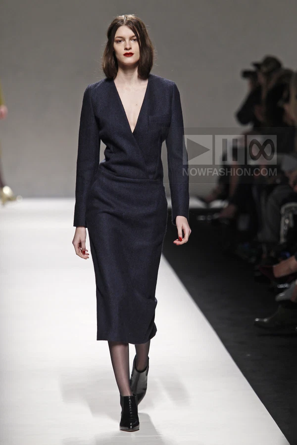 A model walks the runway in a dark navy wool wrap dress with a deep v-neckline and midi-length skirt.