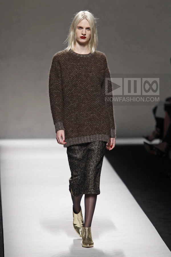 Model wearing a brown textured knit sweater and a dark herringbone pencil skirt with gold metallic ankle boots on runway.