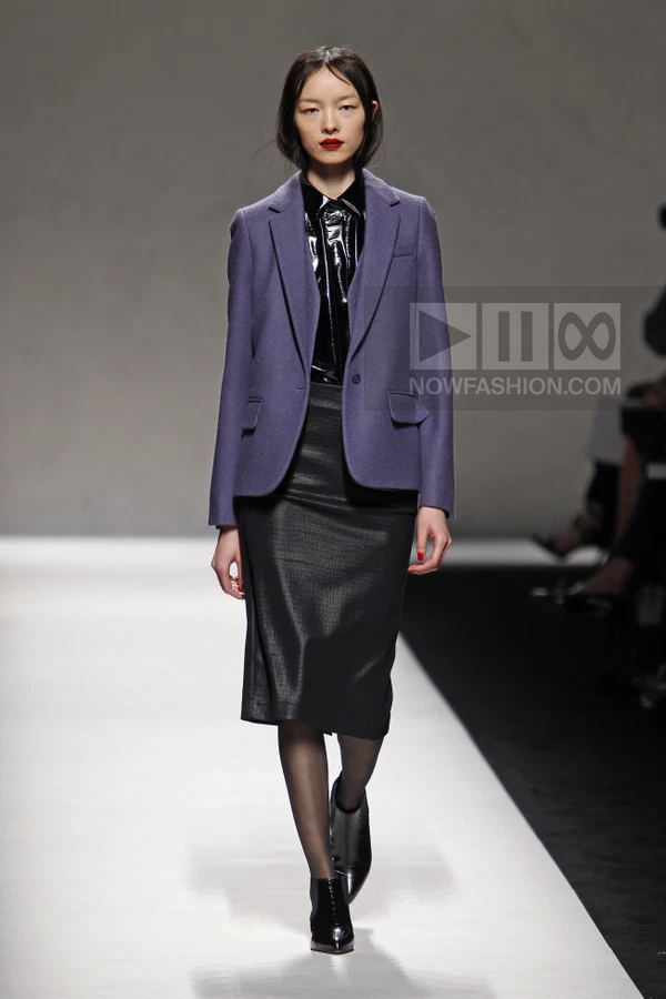 Model wearing a purple wool blazer, black patent shirt, and black textured midi skirt on a runway.