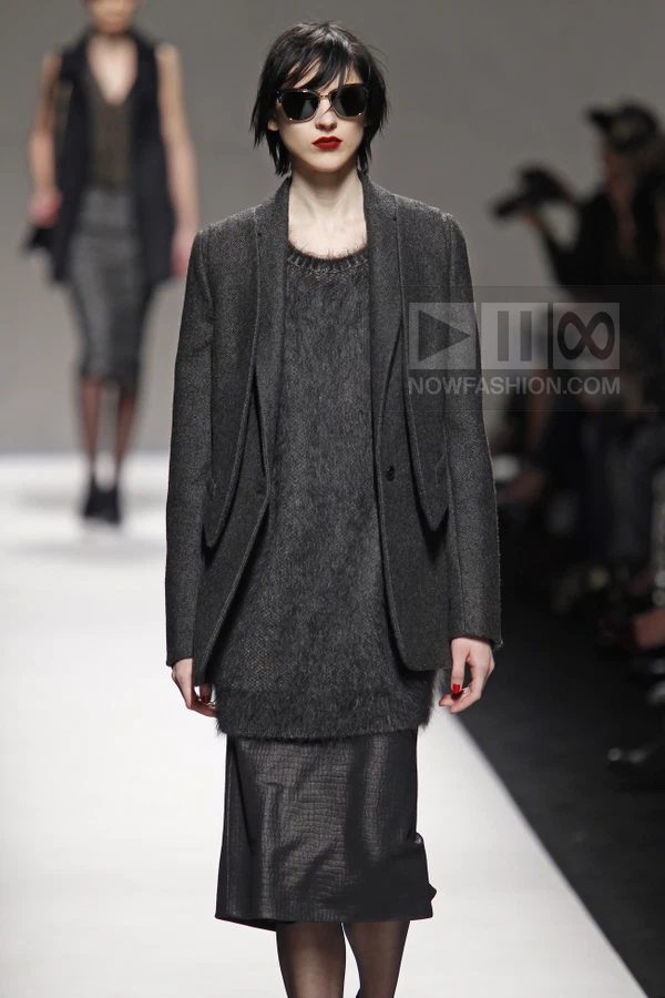 Model wearing a charcoal wool blazer over a fuzzy knit sweater and a dark midi skirt on a runway.
