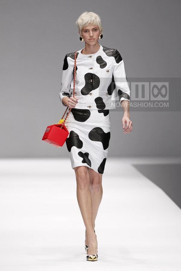 Model walking in a white and black cow-print leather jacket and skirt, carrying a red box-shaped bag with gold chain.
