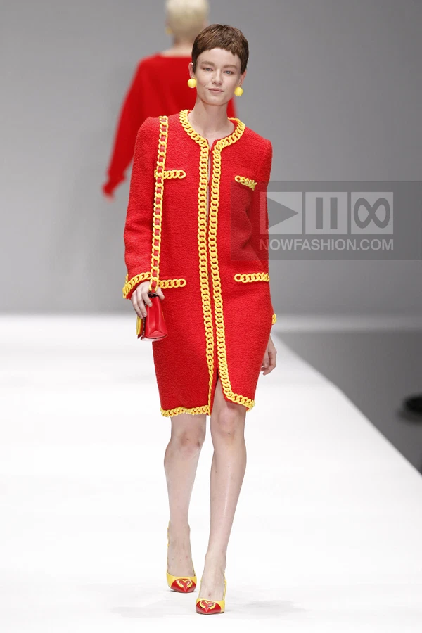 A model walks the runway in a red bouclé coat dress with yellow chain trim, a red shoulder bag, and yellow pumps.