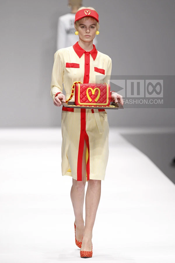 Model wearing a yellow and white striped shirt dress with red trim, a red visor, and carrying a red quilted bag.