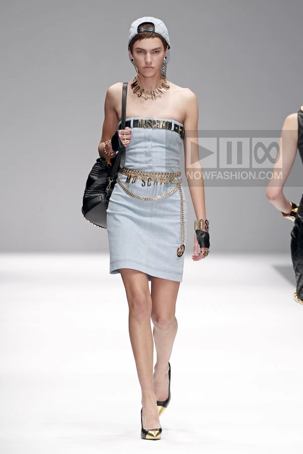 Model wearing a light blue denim strapless mini dress with gold chain belts, a baseball cap, and black leather gloves.