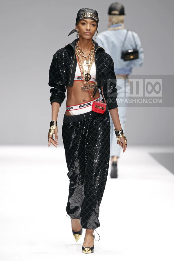 Model walking in a black quilted sequined jacket and matching joggers, white logo underwear, and gold accessories.