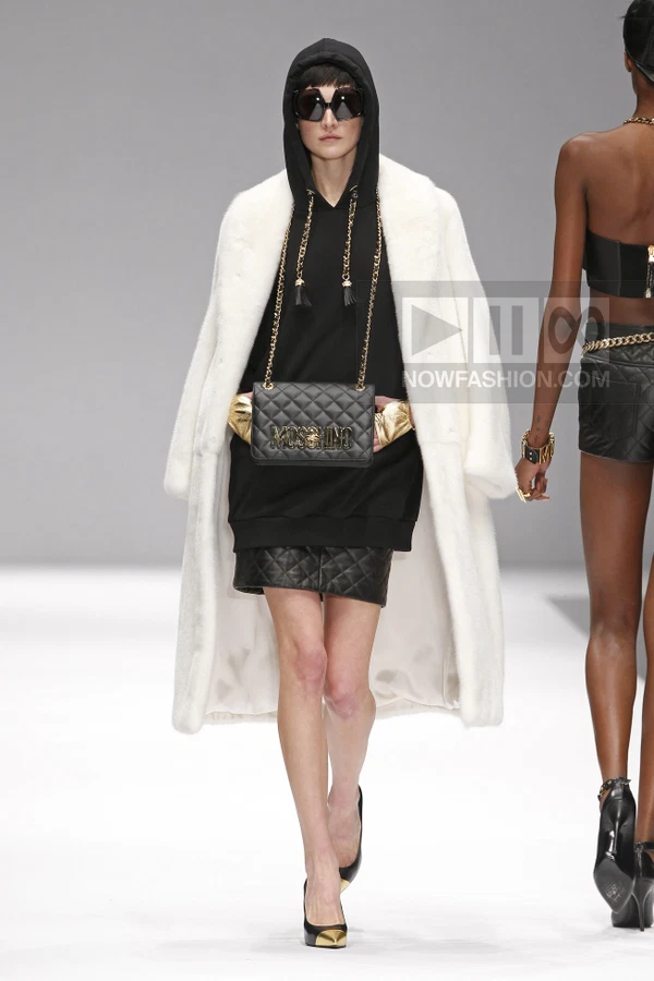 Model wearing a white faux fur coat over a black hooded sweatshirt, quilted skirt, and gold-accented black pumps.