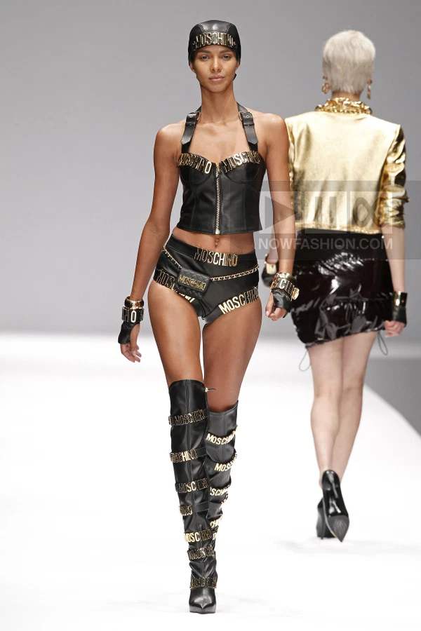 Model wearing a black leather bustier, matching shorts with a mini bag, and knee-high boots with gold logo hardware.