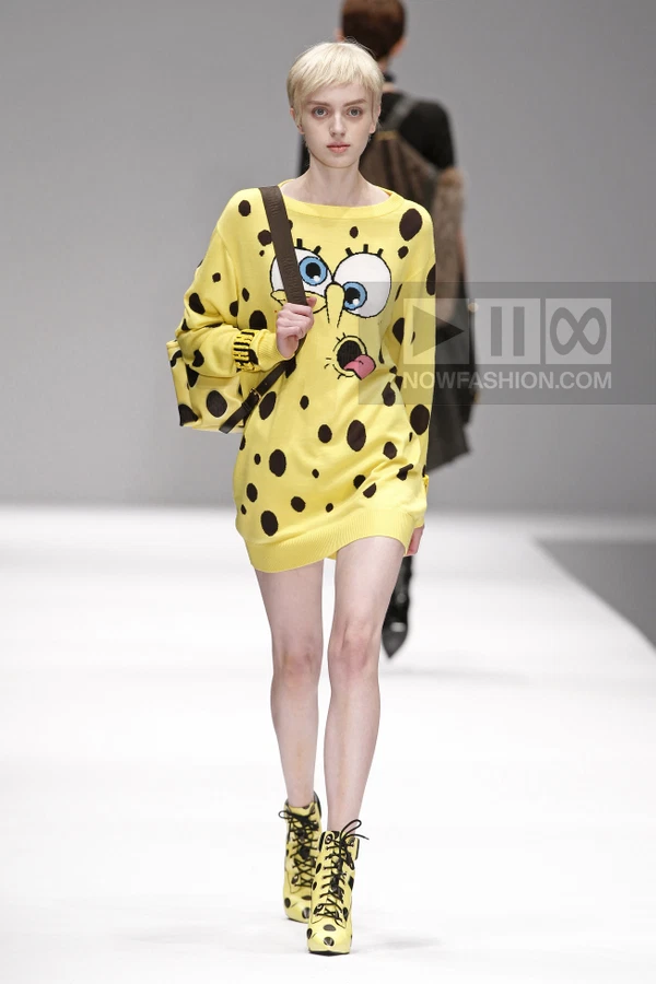 Model wearing a yellow knit sweater dress with a cartoon face graphic and black spots, paired with matching lace-up boots.