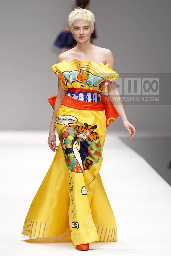 Model wearing a bright yellow strapless gown with a cartoon character print and ruffled bodice on a runway.