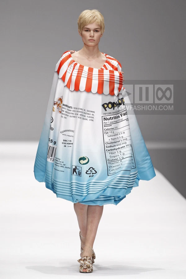 Model wearing a structured, bubble-shaped dress printed with a snack food nutrition label and red-and-white striped trim.