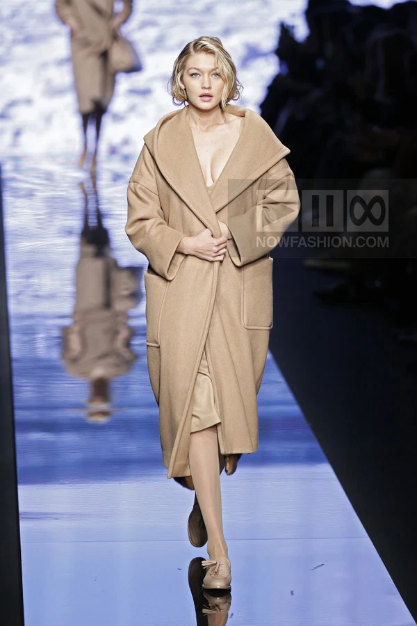 Model walking on a runway wearing a camel-colored hooded wool coat over a matching dress and loafers.