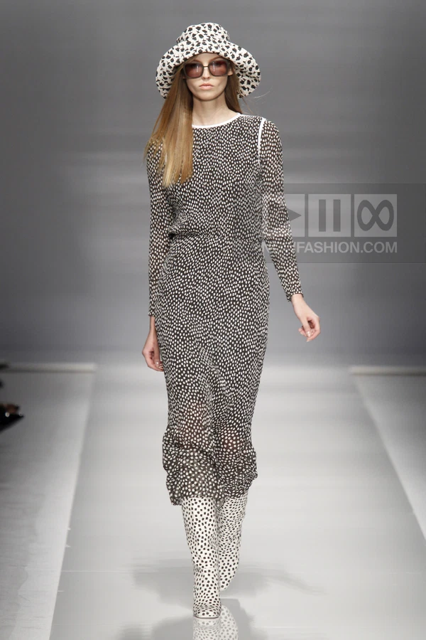 Model on runway wearing a black and white polka-dot midi dress, matching bucket hat, and matching knee-high boots.