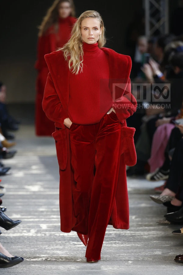 Model walking in a monochromatic red ensemble featuring a long faux fur coat, ribbed turtleneck sweater, and velvet pants.