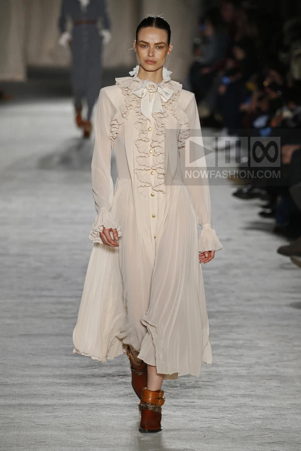 Model wearing a cream-colored chiffon midi dress with ruffled bodice, lace collar, and brown leather ankle boots.
