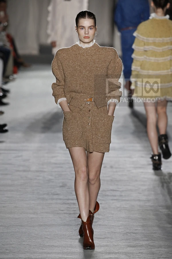 Model walking in a brown knit sweater and matching mini skirt with lace trim and brown leather ankle boots.