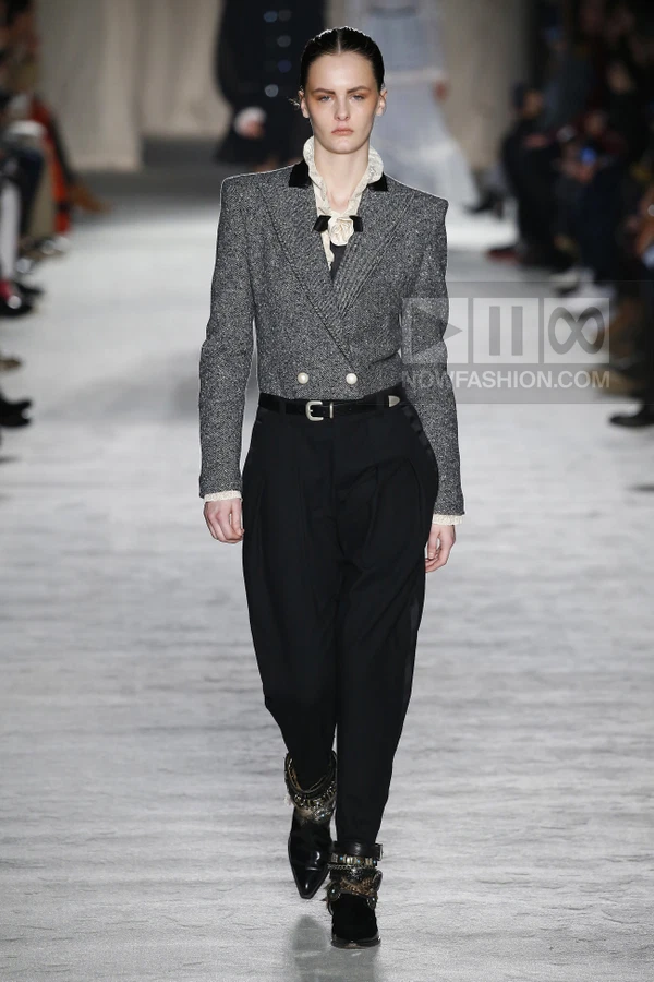 Model walking in a gray tweed double-breasted jacket, black trousers, and black ankle boots on a runway.
