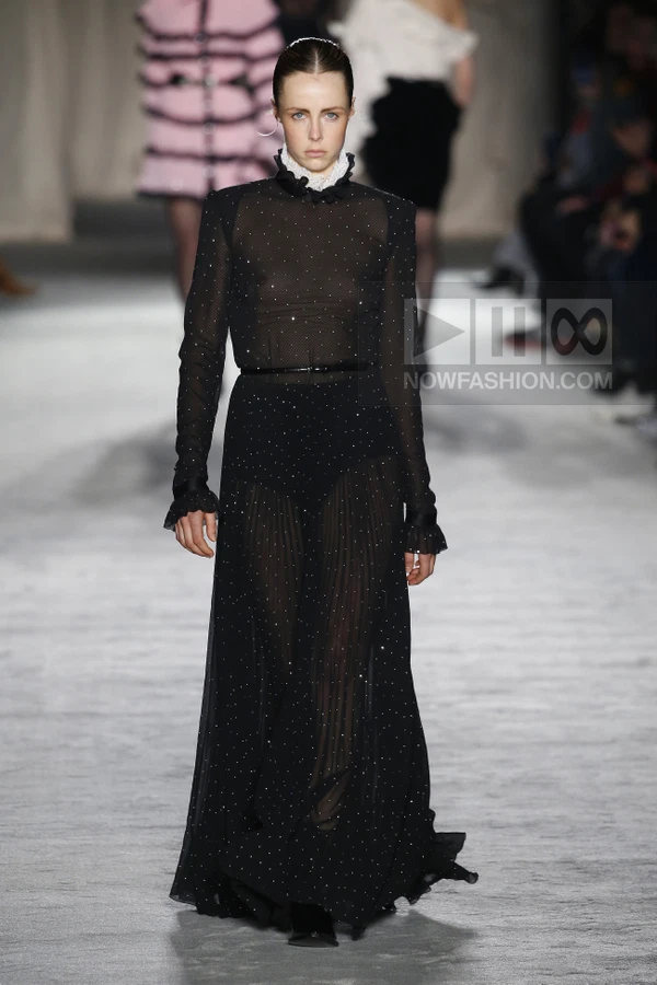 A model walks the runway in a black sheer long-sleeved dress with white polka-dot embellishments and a ruffled collar.