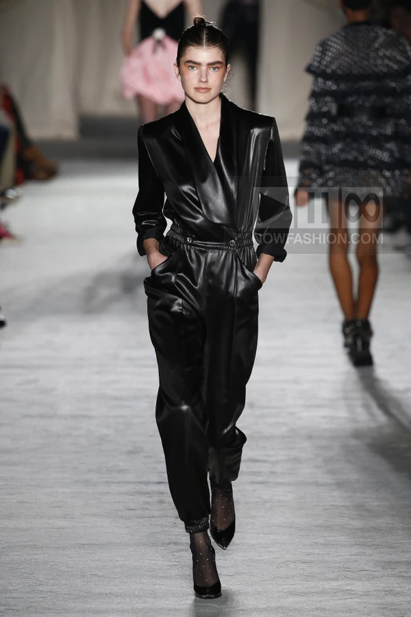 A model walks the runway wearing a black satin jumpsuit with a cinched waist and tapered legs.