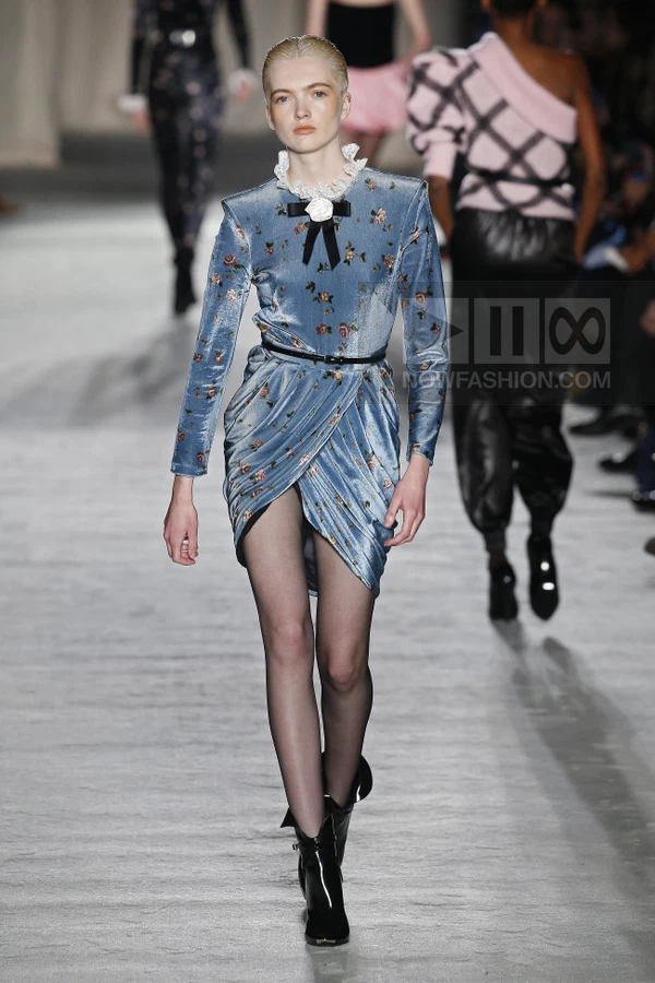 Model walking in a blue velvet floral mini dress with a white lace collar, black bow, and black ankle boots.