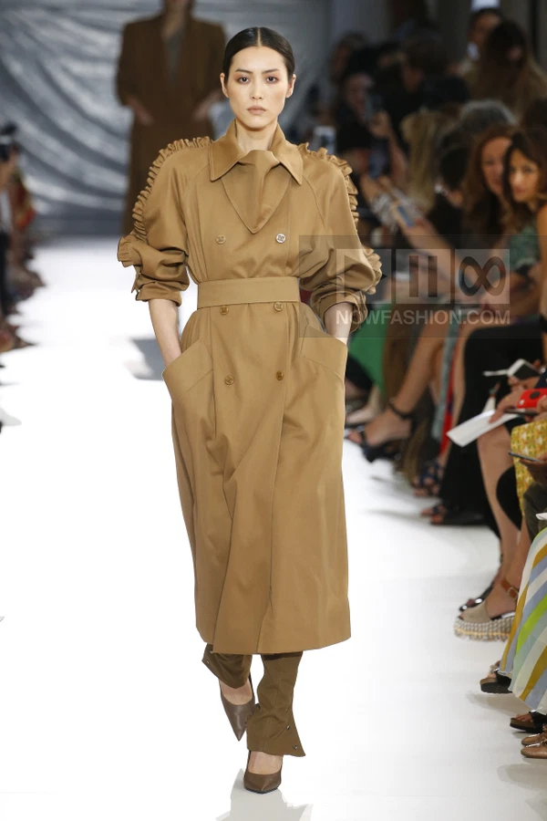 A model walks the runway in a camel-colored double-breasted trench coat with ruffled sleeves and a cinched waist.