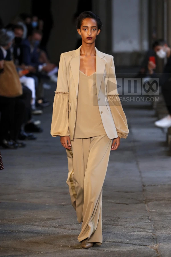 Model walking in a beige blazer with balloon sleeves, matching camisole, and wide-leg trousers on a stone runway.